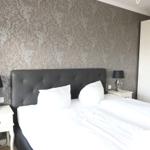 Schlafzimmer mit Bett, Nachttischen und Tapete. Weiße Kleidung und schwarze Lampen.