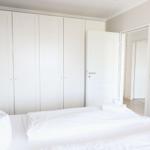 Schlafzimmer mit weißem Bett, Kleiderschrank und Tür zum Flur.