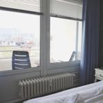 Zimmer mit Blick auf Balkon und Stadt. Bett, Nachttisch und Heizung sichtbar.