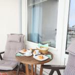 Terrasse mit Tisch, zwei Stühlen und Frühstückszubehör.