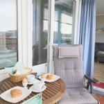 Balkon mit Tisch, Stuhl und Frühstück. Blick ins Wohnzimmer.