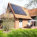 Haus mit Solaranlage, Terrasse und Garten. Holzterrasse und grüner Rasen.