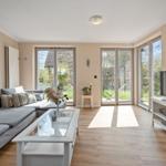 Wohnzimmer mit Sofa, Glas-Tisch und TV. Große Fenster mit Blick auf Garten.