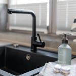 Schwarzes Waschbecken mit modernem Wasserhahn und Seifenflasche auf Arbeitsplatte.