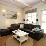 Living room with leather sofa, white table, and wooden floor. Windows and door provide ample light.