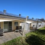 Holiday home with solar panels and terrace with lounge chairs under awning.