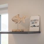 Holzfigur eines Fisches und Schild mit Schrift stehen auf einer Wandregal.