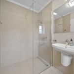 Dusche mit Glaswand, Waschbecken und Spiegel. Fliesenwand und Boden.