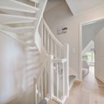 Helle Treppe mit weißer Balustrade führt zur Wohnung. Durch Tür ist Schlafzimmer mit Fenster sichtbar.