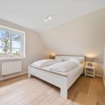 Schlafzimmer mit Doppelbett, Holzboden und Fenster mit Blick auf Grünfläche.