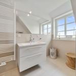 Badezimmer mit Waschbecken, Spiegel und Fenster. Weiße Einbauküche und Heizung.