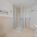 Badezimmer mit Dusche, Waschtisch und Heizung. Wandbild und Haken sichtbar.