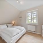 Schlafzimmer mit Dachschräge, weißem Bett, Holzboden und Fenster mit Blick auf Außenbereich.