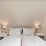 Schlafzimmer mit Doppelbett, zwei Nachttischen und Lampen unter schrägen Decken.