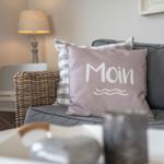 Graue Couch mit Kissen, das Moin schreibt, und einer Lampe im Hintergrund.
