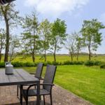 Terrasse mit Tisch und Stühlen. Blick auf grünes Feld und Bäume.