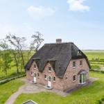 Haus mit Strohdach, Backsteinfassade und Garten. Umgeben von Wiesen und Bäumen.