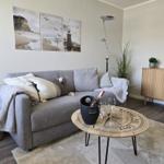 Gray sofa with cushions and blanket, round table with champagne and wall art with lighthouse.
