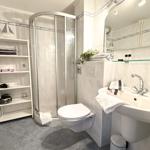Bathroom with shower, sink, and toilet. Shelf with towels and decor.