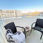 Balcony with two chairs, a small table, and a blanket. View of buildings and sky.