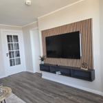 Living room with TV wall, wood paneling, and dark console. Wood floor and white walls.