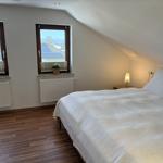 Schlafzimmer mit Dachschräge, zwei Fenstern und Holzboden. Bett mit weißer Bettwäsche.