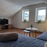Wohnzimmer mit Sofa, Fernseher und zwei Fenstern.