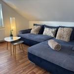 Ein Wohnzimmer mit blauem Sofa, Tisch und Lampe. Holzfußboden und Fenster mit Jalousie.