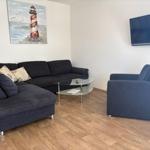 Wohnzimmer mit Sofa, Sessel, Glas-Tisch und Wandbild. Fernseher an der Wand.