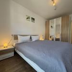 Schlafzimmer mit Doppelbett, Nachttisch und Kleiderschrank. Badezimmer mit Dusche ist sichtbar.