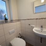 Badezimmer mit Waschbecken, Spiegel, Toilette und Fenster mit Pflanze.