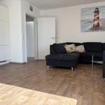 Wohnzimmer mit Sofa, Holzboden und Leuchtturm-Bild an der Wand.