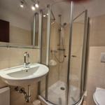 Badezimmer mit Dusche, Waschbecken und Toilette. Fliesenwand und Spiegel.