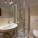 Badezimmer mit Dusche, Waschbecken und Toilette. Fliesenwand und Spiegel.