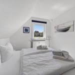 Schlafzimmer mit Dachschrägen, Bett, Fenster und Wandbildern.