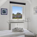 Schlafzimmer mit Blick auf Häuser und Himmel. Bett mit Handtüchern. Wandbild und Fenster.
