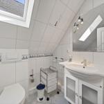Badezimmer mit Toilette, Waschbecken und Dachfenster. Wandfliesen mit Segelyacht-Motiv.