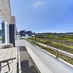 Terrasse mit Tisch und Stühlen. Blick auf grüne Hügel und Ferienhäuser.