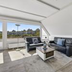 Wohnzimmer mit zwei schwarzen Sofas, Tisch und Blick auf Wohnhäuser.