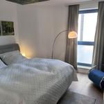 Schlafzimmer mit Bett, Stehlampe und blauem Sessel. Fenster mit Vorhängen.