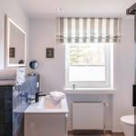 Bathroom with sink, shower, and window with striped roller blind.