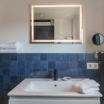 Bathroom with blue tiles, mirror, and towel radiator.