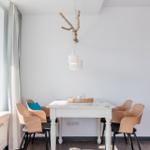Dining room with white table, wooden chairs, and hanging lamp with branch.