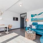 Living room with blue sofa, dining table, and wall art. Wood floor and ceiling light.