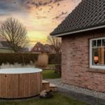 Haus mit Holzwhirlpool im Garten bei Sonnenuntergang.