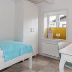 Schlafzimmer mit weißem Bett, Schrank und Schreibtisch. Fenster mit gelbem Jalousie.