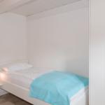 Ein Schlafzimmer mit Einzelbett, weißer Wand und Kleiderschrank.