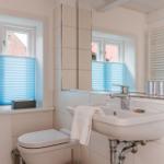 Badezimmer mit Waschbecken, Spiegel, Toilette und Fenster mit blauen Jalousien.