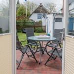 Terrasse mit Tisch und Stühlen, Blick auf Garten und Haus mit Strohdach.