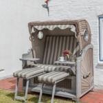Ein bequemer Strandkorb mit Sitzbank und Fußstützen steht auf einem gepflasterten Platz.